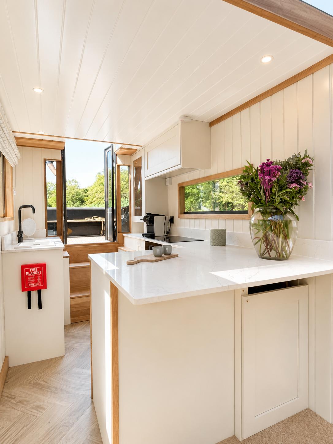 Theta galley with pale cabinetry, white worktops, flowers and glazed rear doors